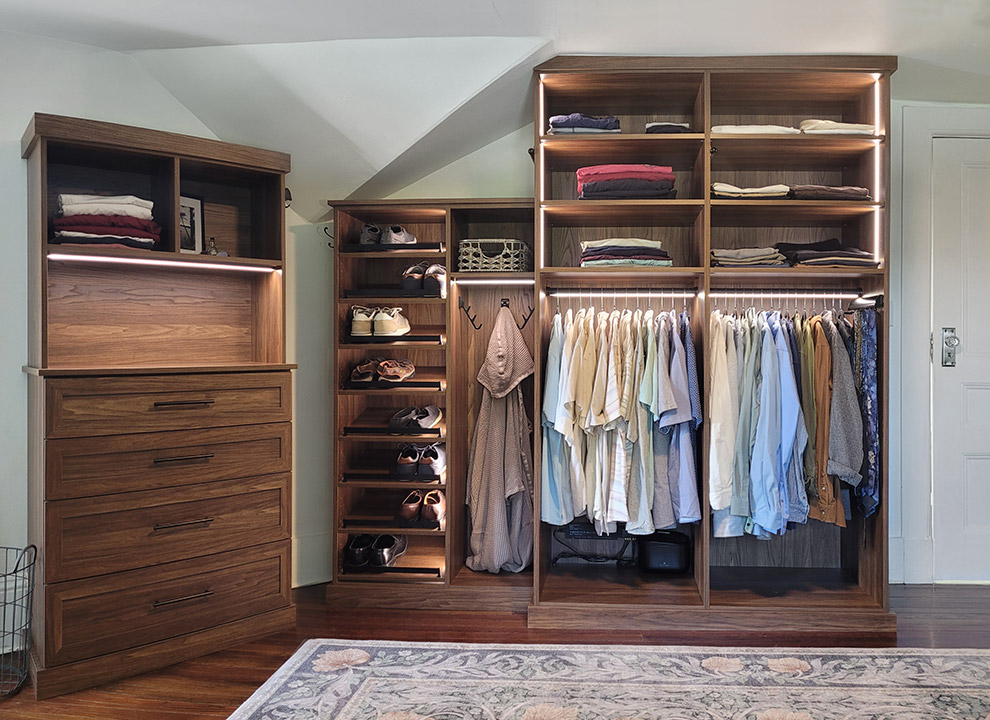 Angled Wall Shared His and Hers Closet with Built-In Bureau Cabinet with Integrated Lighting and His Closet with Shoe Storage, Valet Rods & Lighted Hanging Rods